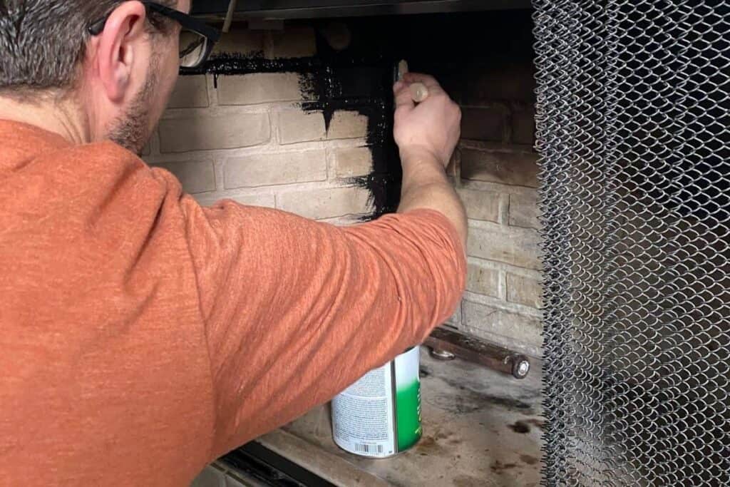 Man using brush to paint inside of fireplace with black high heat paint