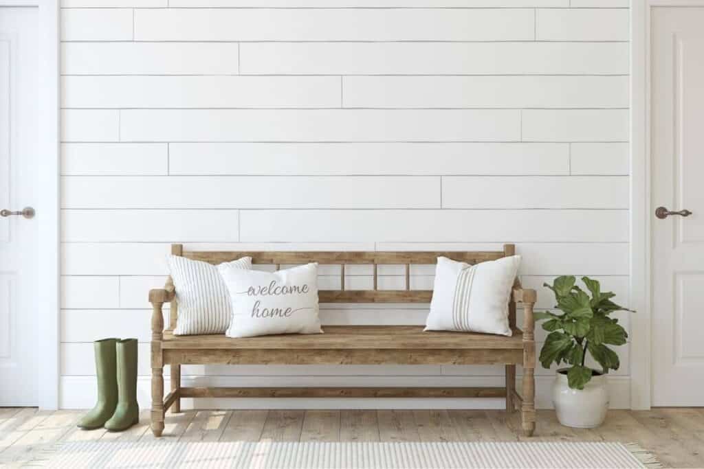 Farmhouse style white shiplap with wood bench and cream colored pillows