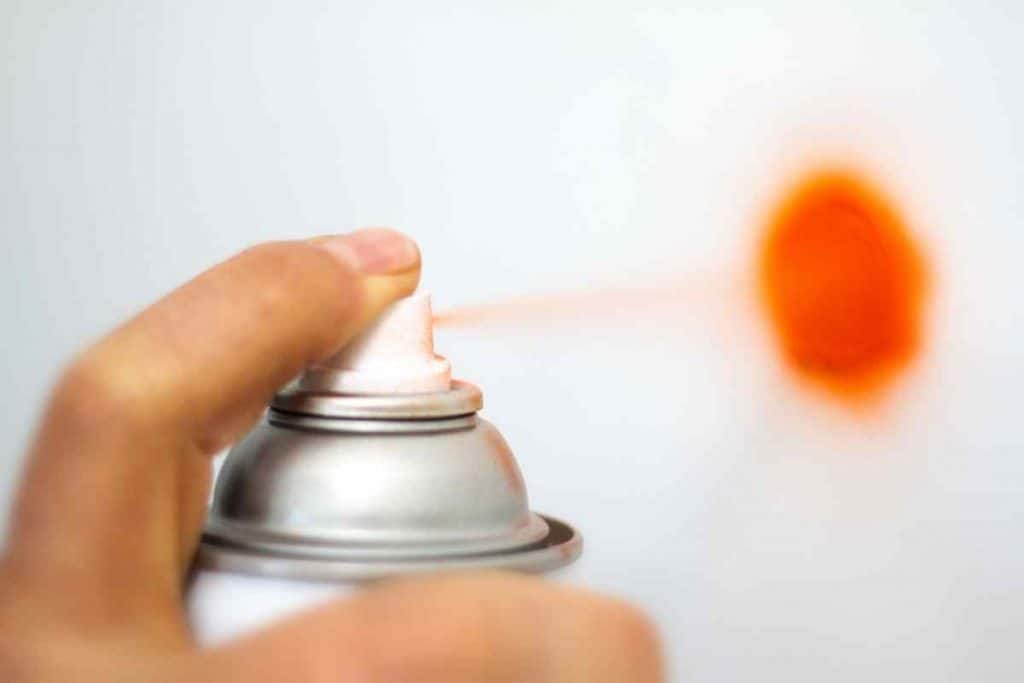 finger on nozzle of spray paint can spraying orange paint
