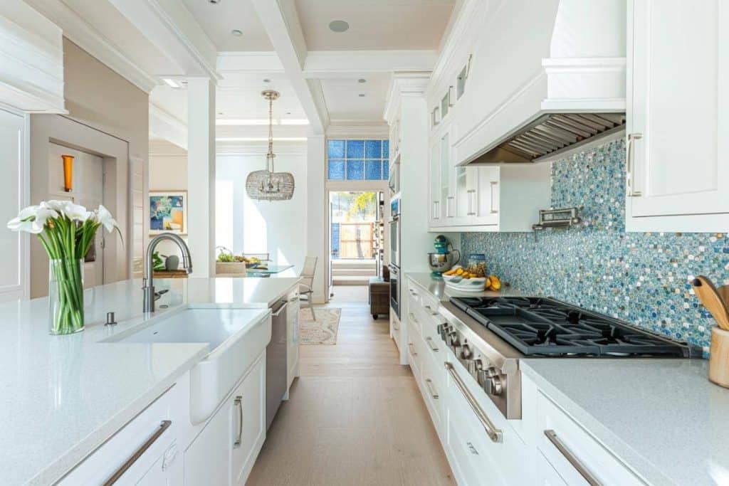 An elegant kitchen with serene blue cabinets, white countertops, and a distinctive blue mosaic tile backsplash that adds a pop of color.