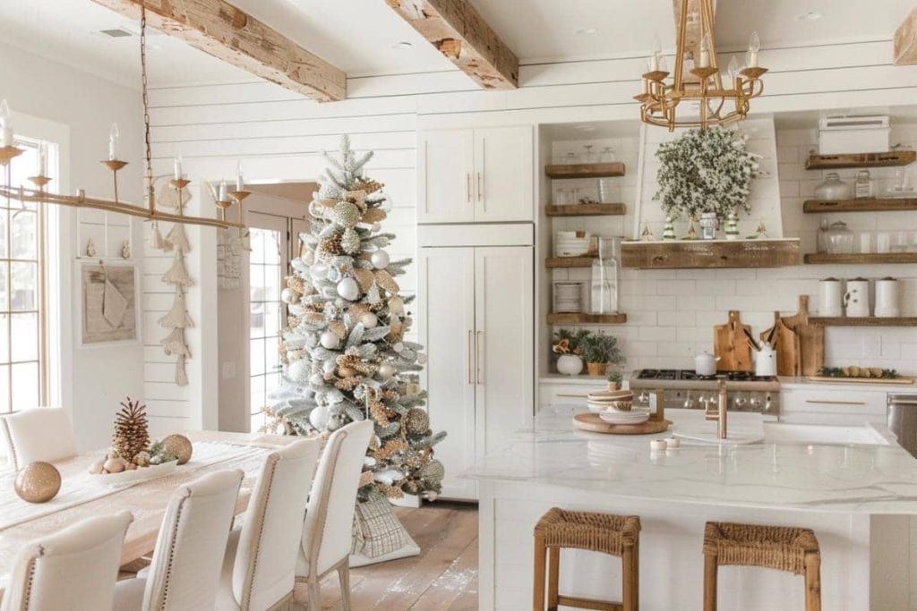 A serene farmhouse kitchen with a white color scheme, featuring a large Christmas tree adorned with white and silver ornaments, complemented by rustic wooden shelves and a chandelier