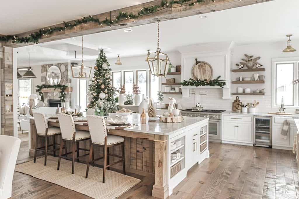 Bright and airy farmhouse kitchen with Christmas decorations, featuring a large festive tree, a dining table with upholstered chairs, and elegant lighting fixtures