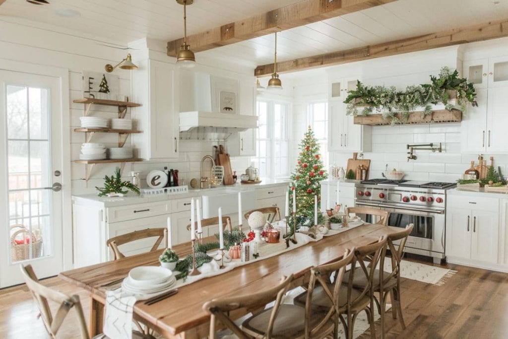 Rustic farmhouse dining area with a long wooden table set for Christmas, a vibrant tree in the corner, and a kitchen with white cabinetry and open shelving in the background