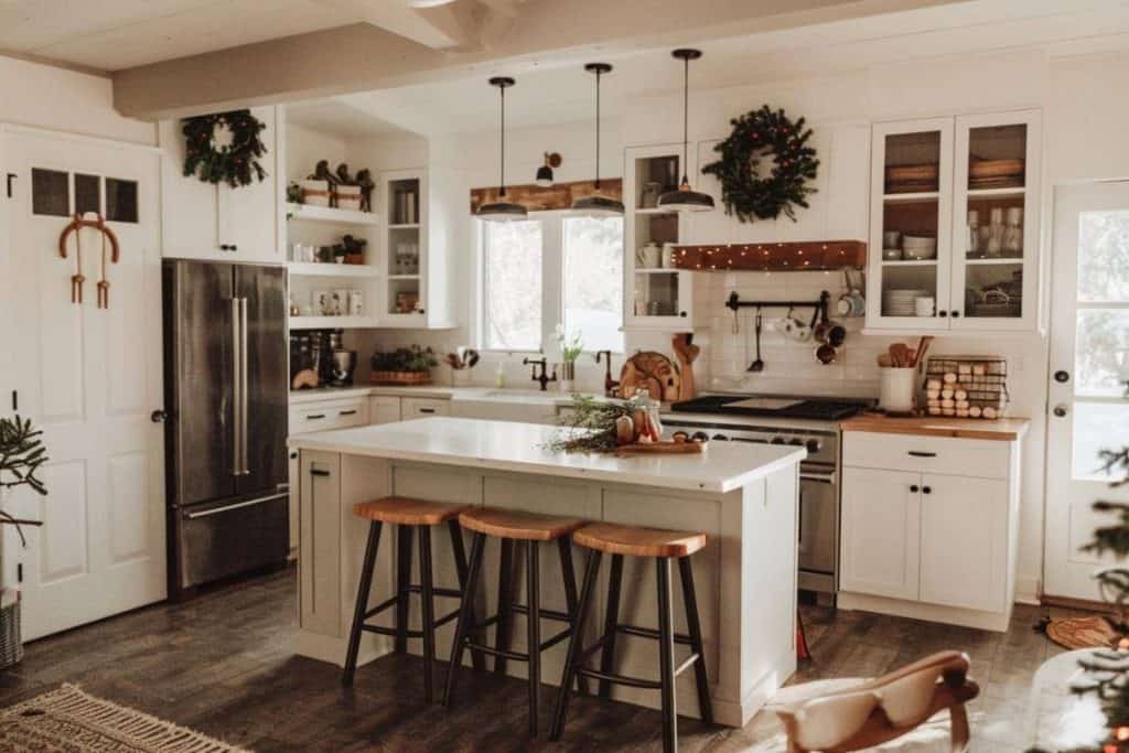 Warmly lit farmhouse kitchen with a central island, Christmas wreaths, and garlands.