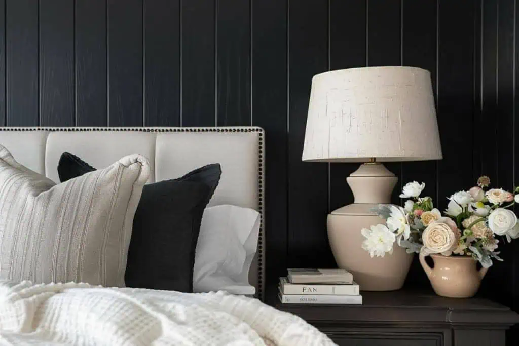 Black and neutral bedroom with a sophisticated table lamp, a bouquet of flowers, and a curated selection of books on a nightstand.