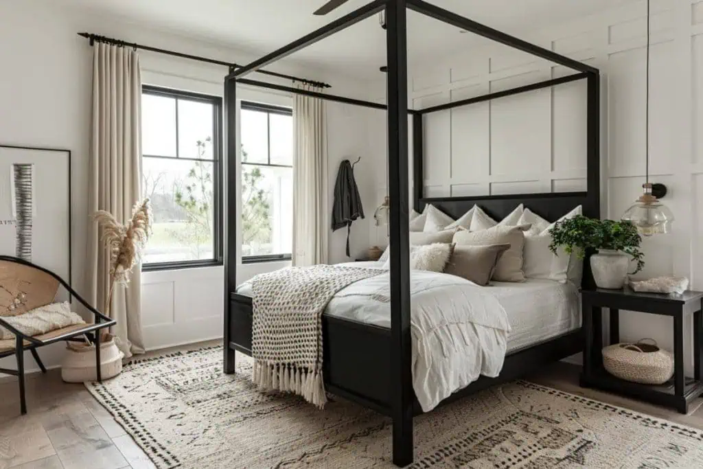 A spacious black and neutral bedroom featuring a black four-poster bed with white bedding and a mix of beige and gray pillows, a natural woven rug, and a cozy armchair with a pampas grass arrangement
