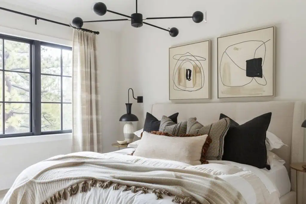 Modern black & neutral bedroom featuring a beige upholstered bed with a variety of textured pillows, abstract wall art, and a stylish sputnik light fixture overhead