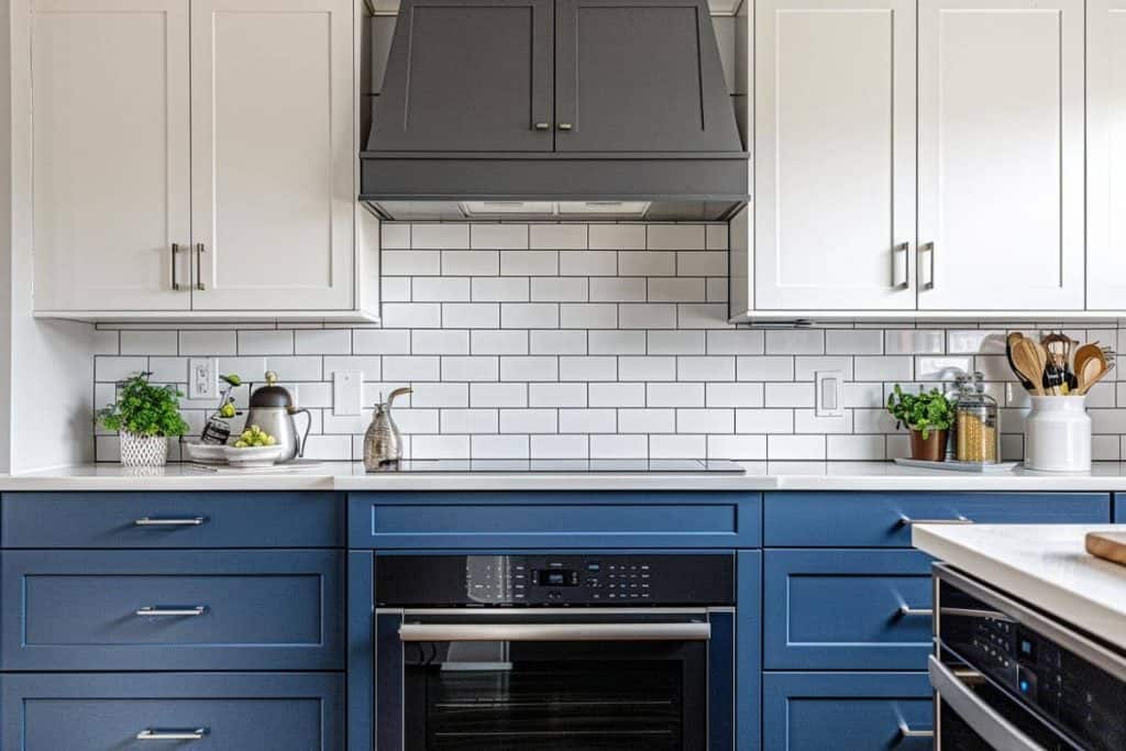 Modern farmhouse kitchen with sleek two-toned cabinets, dark blue lower cabinets and white upper cabinets, accented with subway tiles and gold hardware
