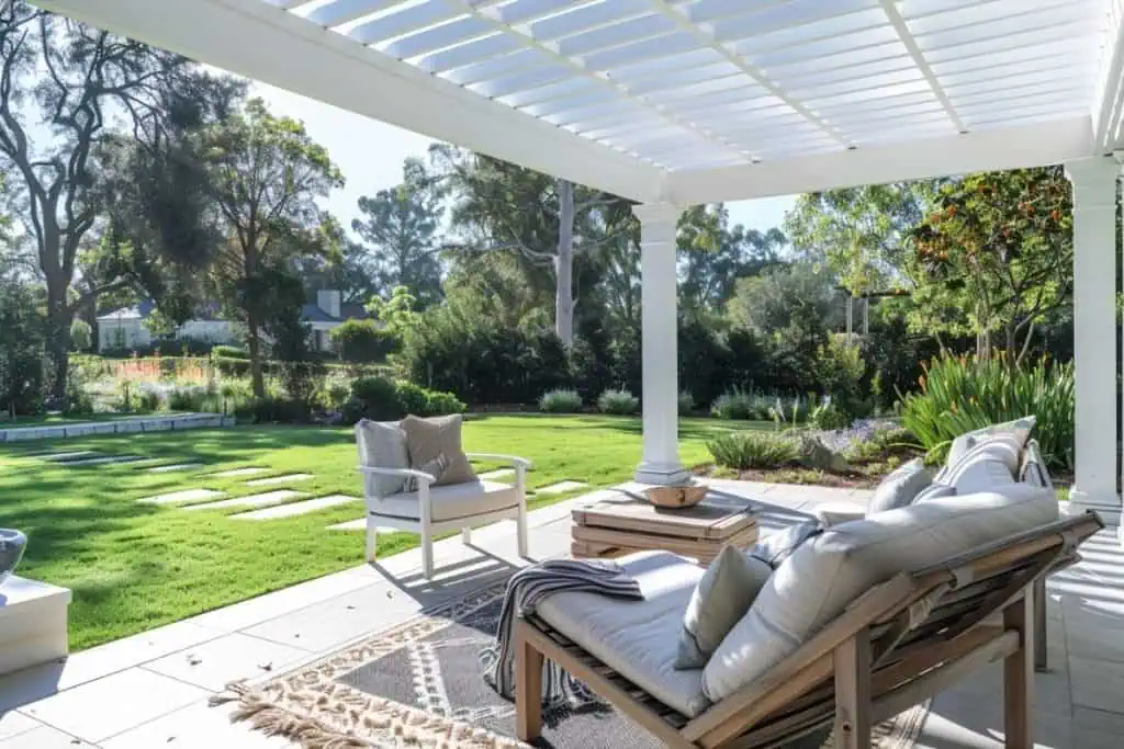 A bright and airy patio with a white pergola, comfortable seating, and a lush garden in the background.
