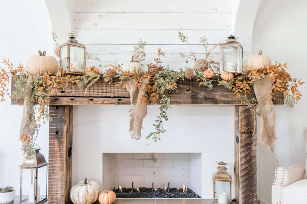 Rustic wooden mantle decorated for fall with white pumpkins, dried foliage, and burlap ribbons, creating a cozy autumnal atmosphere.