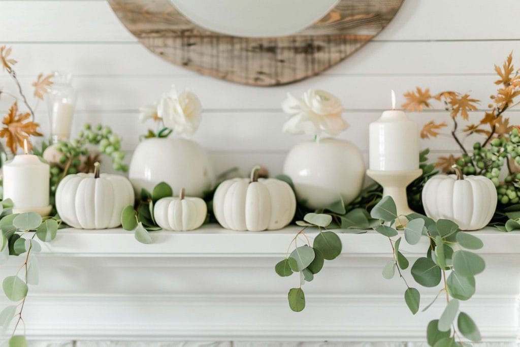 White pumpkins, eucalyptus leaves, and white candles on a white mantle, reflecting a minimalist and elegant fall decor.