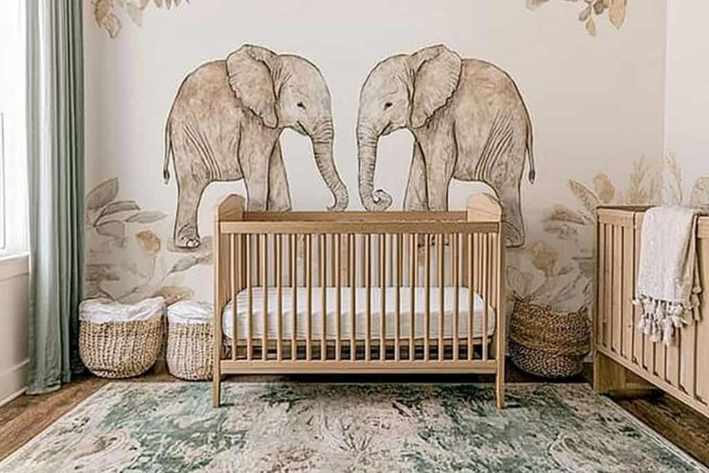 A whimsical girl nursery with an elephant-themed mural, a light wooden crib, and soft, nature-inspired decor. Wicker storage baskets sit on a textured green and cream rug.